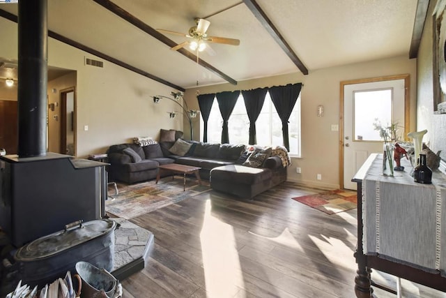 living room with lofted ceiling with beams, ceiling fan, a wood stove, and dark hardwood / wood-style flooring