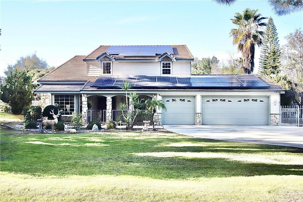 view of front of house featuring a garage, covered porch, a front yard, and solar panels