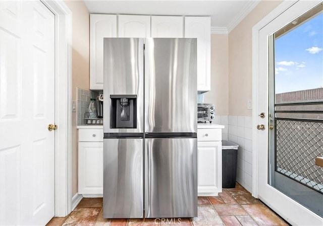 kitchen with ornamental molding, white cabinets, tile walls, and stainless steel fridge