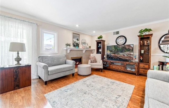 living room with light wood-type flooring, crown molding, and a tiled fireplace