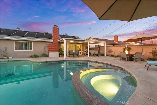 pool at dusk featuring an in ground hot tub and a patio