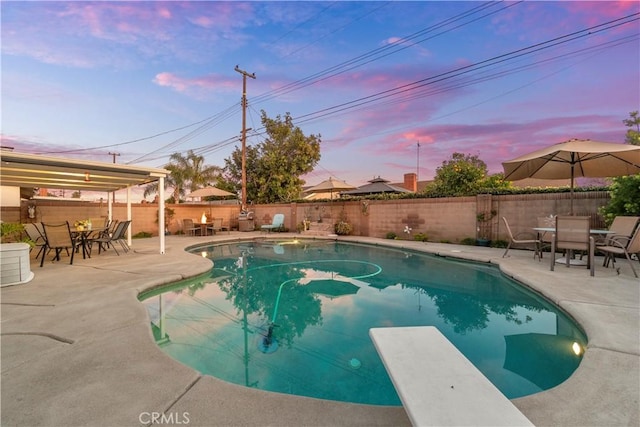 pool at dusk featuring a diving board and a patio area