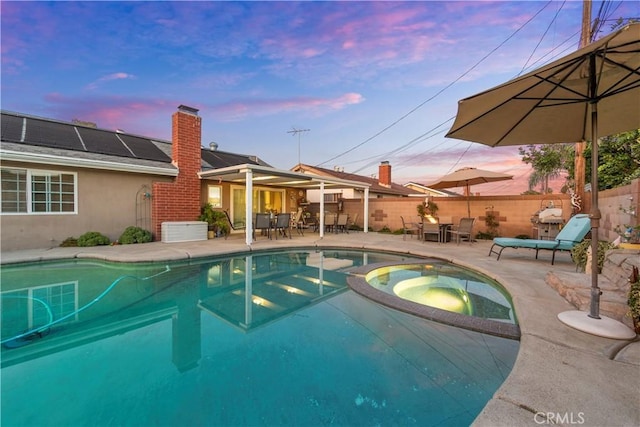 pool at dusk featuring a patio and an in ground hot tub