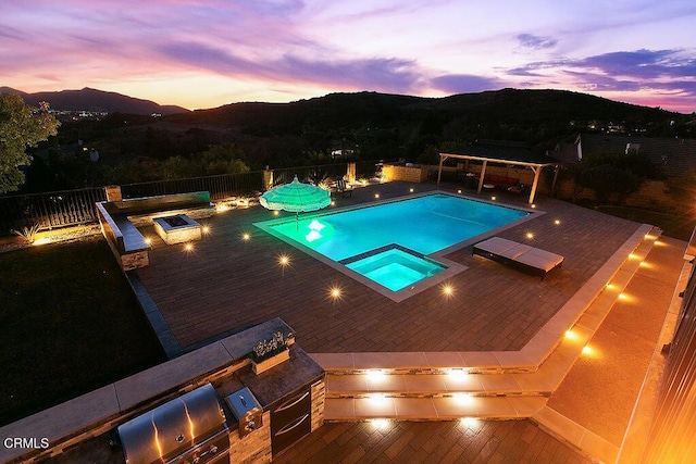 pool at dusk featuring area for grilling, a mountain view, a patio area, and an in ground hot tub