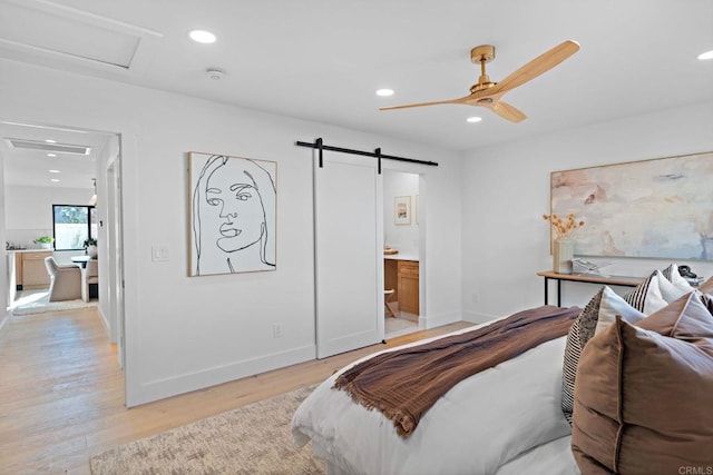 bedroom featuring connected bathroom, a barn door, and light hardwood / wood-style flooring