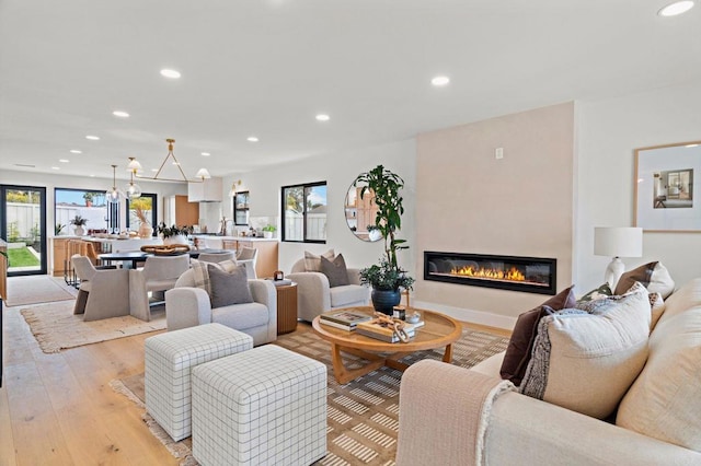 living room with a notable chandelier, plenty of natural light, a fireplace, and light wood-type flooring