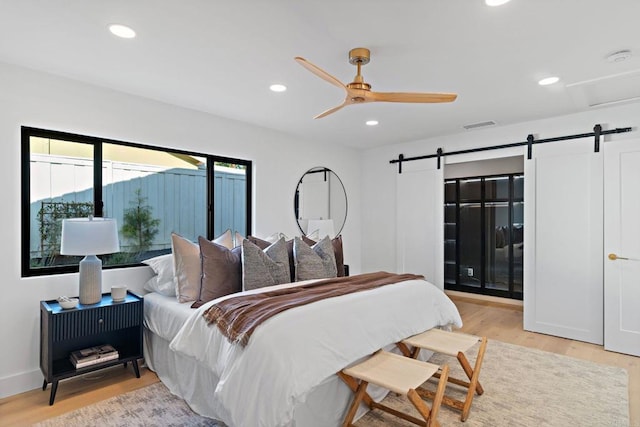 bedroom featuring ceiling fan, a barn door, and light hardwood / wood-style floors