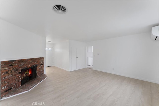 unfurnished living room with an AC wall unit, a brick fireplace, and light hardwood / wood-style flooring