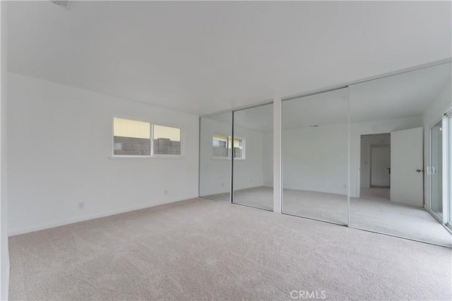 unfurnished bedroom featuring light colored carpet and multiple closets