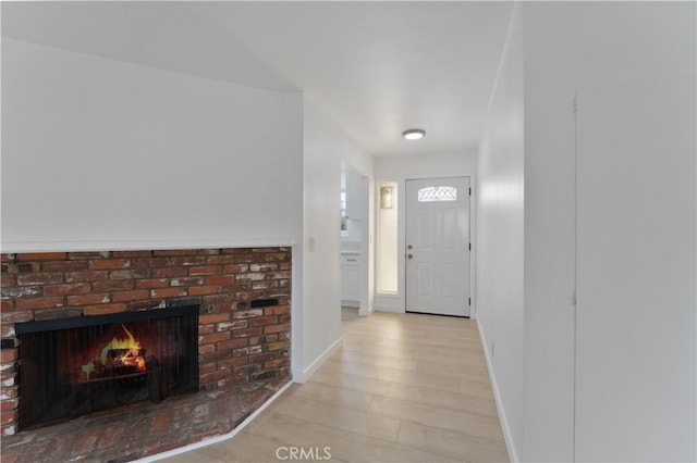 foyer entrance with a brick fireplace and light wood-type flooring