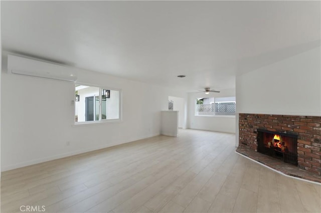 unfurnished living room with ceiling fan, a fireplace, a wall mounted AC, and light wood-type flooring