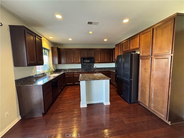 kitchen featuring dark stone countertops, a center island, dark wood-type flooring, and black appliances