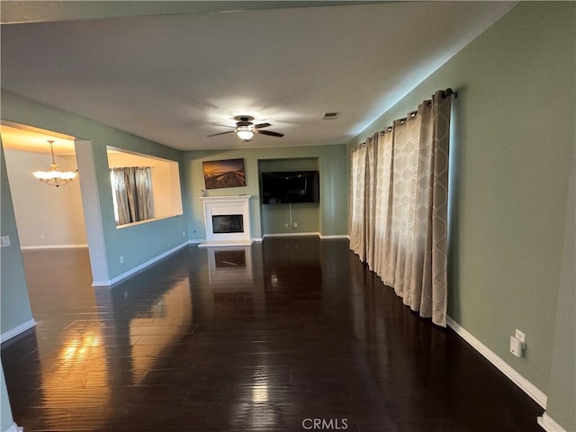 unfurnished living room featuring dark wood-type flooring and ceiling fan with notable chandelier