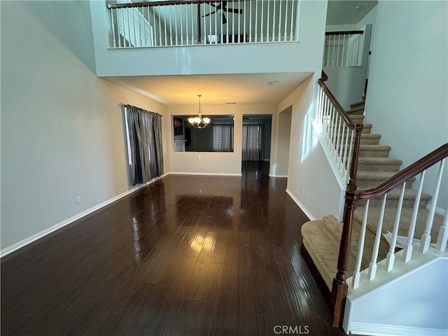 unfurnished living room with dark wood-type flooring, a notable chandelier, and a towering ceiling