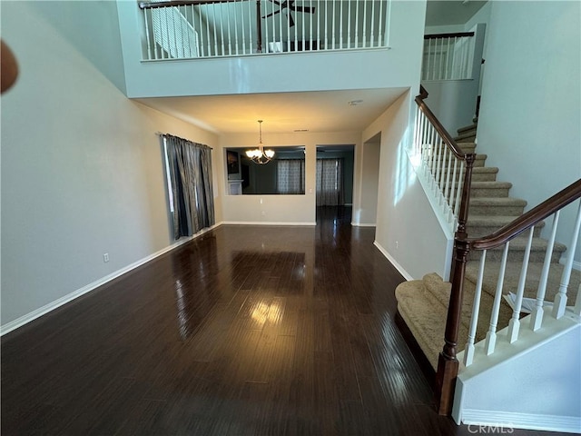 unfurnished living room featuring dark wood-type flooring, a chandelier, and a high ceiling