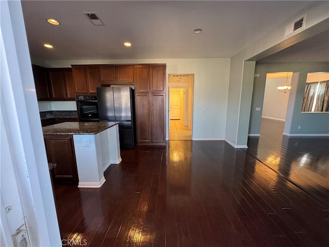 kitchen featuring fridge, dark hardwood / wood-style floors, dark stone countertops, and black oven