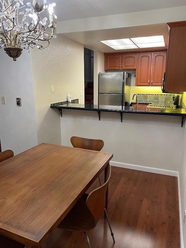 kitchen featuring a breakfast bar, stainless steel refrigerator, backsplash, dark hardwood / wood-style flooring, and kitchen peninsula