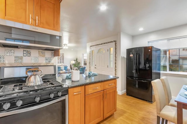 kitchen featuring black refrigerator, range with gas stovetop, decorative backsplash, dark stone counters, and light hardwood / wood-style flooring