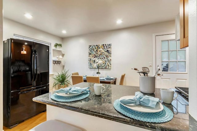 kitchen with black fridge, dark stone counters, kitchen peninsula, and light hardwood / wood-style floors