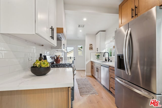 kitchen featuring stainless steel appliances, white cabinetry, sink, and light stone counters