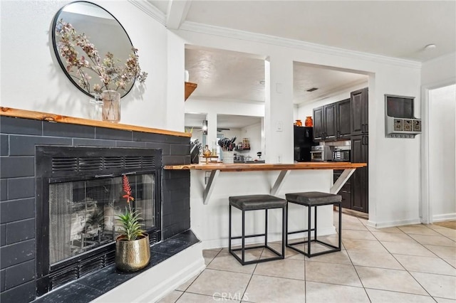 kitchen with dark brown cabinetry, ornamental molding, a kitchen breakfast bar, and black fridge