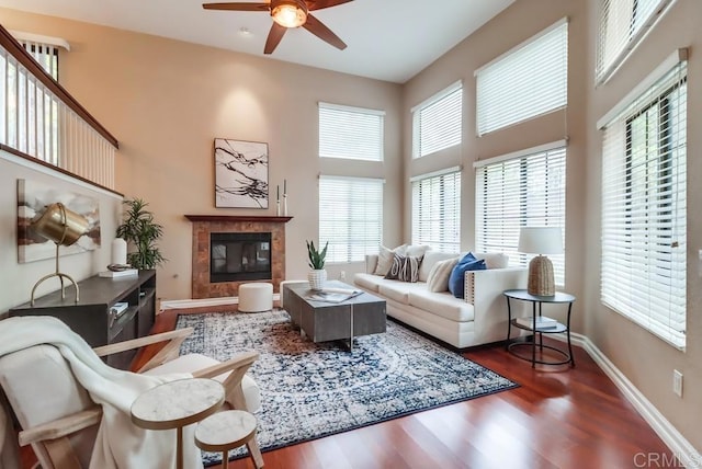 living room featuring ceiling fan, dark hardwood / wood-style flooring, a tile fireplace, and a high ceiling