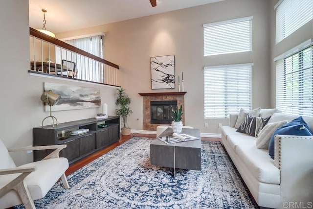 living room featuring a tiled fireplace, a healthy amount of sunlight, a towering ceiling, and hardwood / wood-style floors