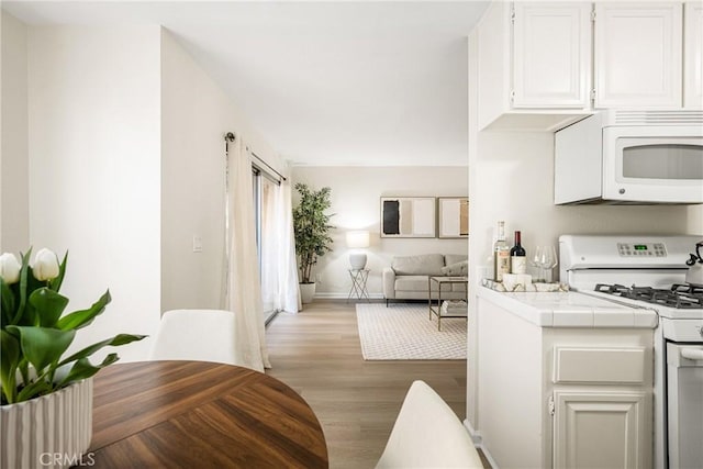 kitchen with white cabinetry, white appliances, tile countertops, and light wood-type flooring