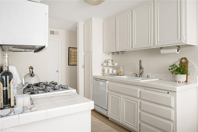 kitchen featuring white dishwasher, sink, white cabinetry, and tile countertops