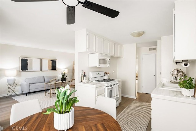 kitchen with sink, white appliances, dark wood-type flooring, tile counters, and white cabinets