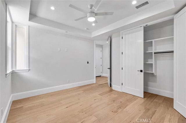 unfurnished bedroom featuring a tray ceiling, a closet, ceiling fan, and light wood-type flooring