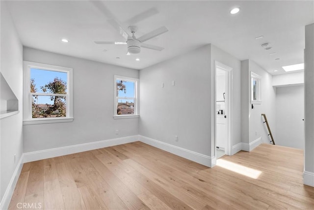 spare room with a skylight, light hardwood / wood-style flooring, and ceiling fan