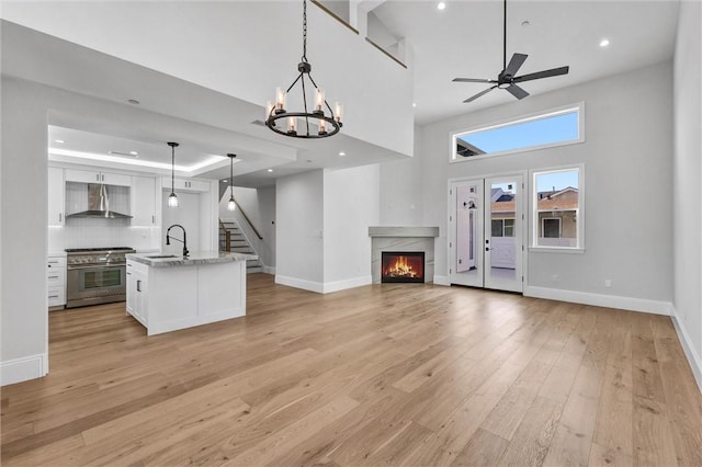 kitchen featuring wall chimney exhaust hood, high end range, an island with sink, pendant lighting, and white cabinets