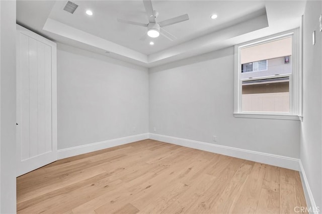 unfurnished room featuring a raised ceiling, ceiling fan, and light wood-type flooring