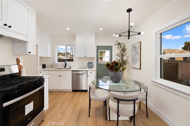 kitchen featuring pendant lighting, sink, white cabinets, stainless steel appliances, and light hardwood / wood-style flooring