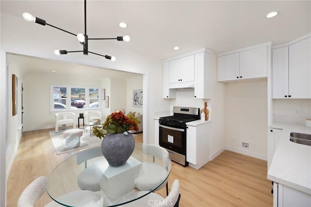 kitchen with sink, stainless steel gas range oven, light hardwood / wood-style floors, white cabinets, and a chandelier