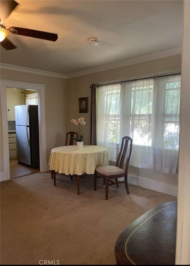 carpeted dining area featuring crown molding and ceiling fan