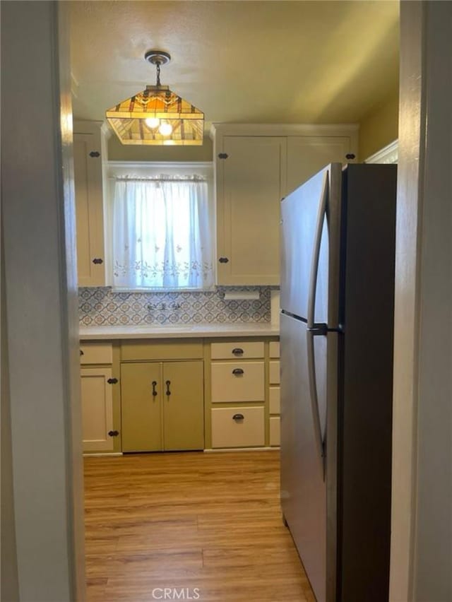 kitchen with decorative backsplash, light hardwood / wood-style flooring, decorative light fixtures, and stainless steel refrigerator