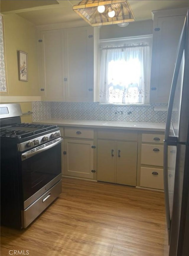 kitchen with light wood-type flooring, gas stove, tasteful backsplash, and white cabinets