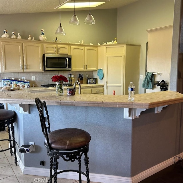 kitchen with pendant lighting, light tile patterned floors, a breakfast bar, tasteful backsplash, and kitchen peninsula