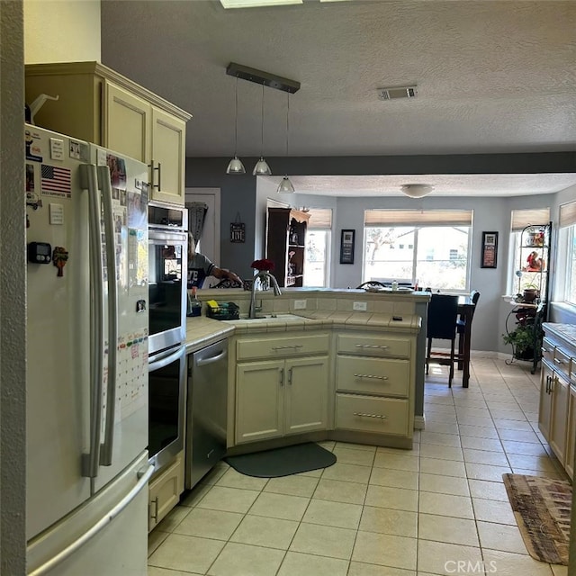 kitchen with light tile patterned flooring, tile countertops, decorative light fixtures, white fridge, and stainless steel dishwasher