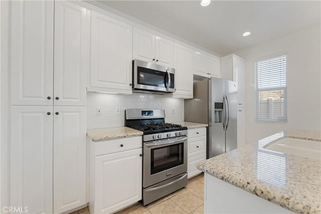 kitchen featuring light tile patterned floors, stainless steel appliances, light stone countertops, decorative backsplash, and white cabinets