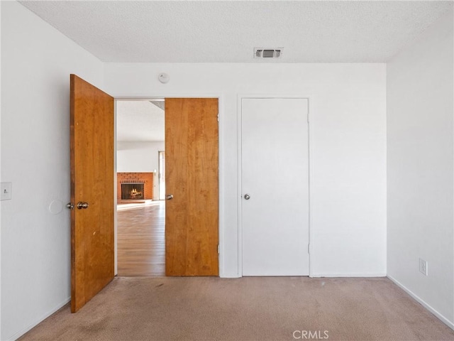 unfurnished bedroom featuring light carpet, a brick fireplace, and a textured ceiling