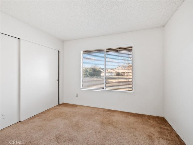 unfurnished bedroom featuring light colored carpet, a closet, and a textured ceiling