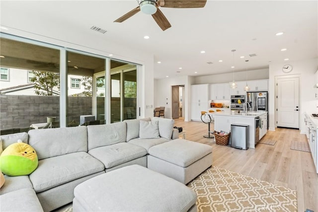 living room with ceiling fan, sink, and light wood-type flooring