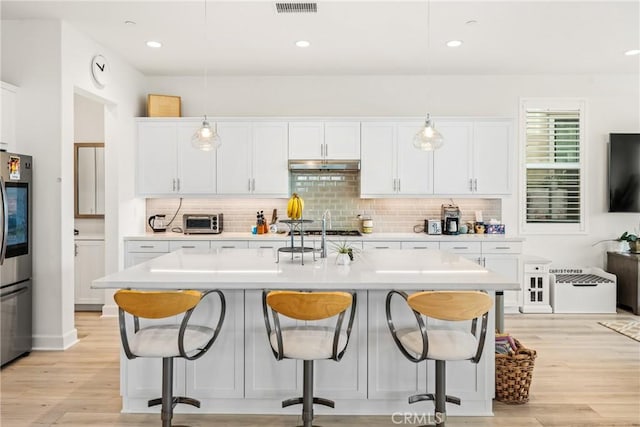 kitchen featuring pendant lighting, stainless steel refrigerator, an island with sink, a breakfast bar area, and white cabinets