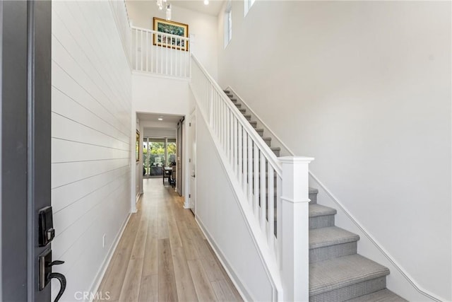 staircase with a high ceiling, wood-type flooring, and wooden walls