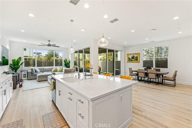 kitchen with white cabinetry, a kitchen island with sink, hanging light fixtures, and light wood-type flooring