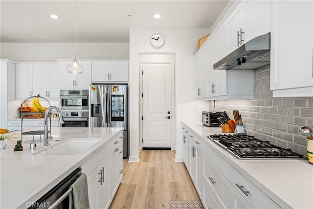 kitchen featuring appliances with stainless steel finishes, pendant lighting, white cabinetry, sink, and light hardwood / wood-style flooring