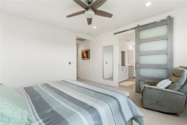 bedroom featuring ensuite bathroom, a barn door, and ceiling fan